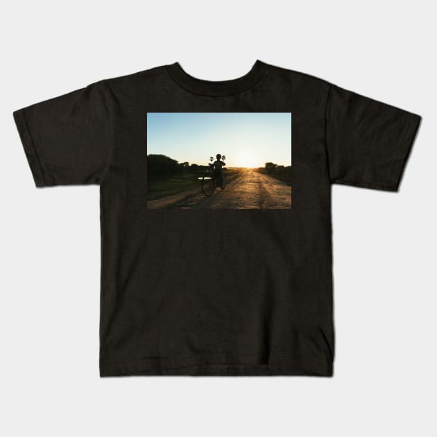 Silhouette of Boy Riding Bicycle at Sunset in Burmese Countryside Kids T-Shirt by visualspectrum